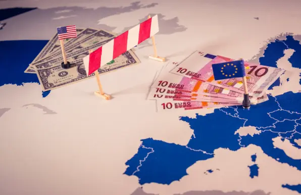Illustration of US–EU trade barriers with American dollars and EU euros separated by a striped barricade on a map of Europe and the USA.