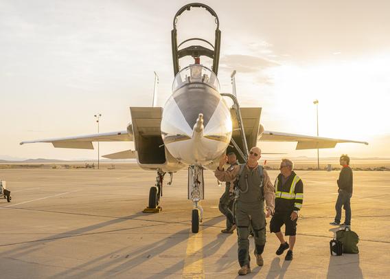 NASA test pilot Nils Larson walks around an F-15B aircraft at NASA’s Armstrong Flight Research Center in Edwards, California. He wears a green G-suit over his tan flight suit and looks up at the nose of the aircraft. The F-15 canopy is open, and support crew stand near the aircraft as the pilots walks around. The aircraft sits higher than the pilot, allowing a partial view of the area on the opposite side. NASA test pilot Nils Larson walks around an F-15B aircraft at NASA’s Armstrong Flight Research Center in Edwards, California. He wears a green G-suit over his tan flight suit and looks up at the nose of the aircraft. The F-15 canopy is open, and support crew stand near the aircraft as the pilots walks around. The aircraft sits higher than the pilot, allowing a partial view of the area on the opposite side.