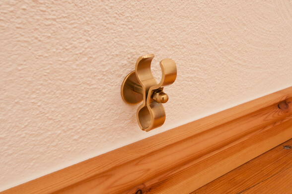 Heizungsrohrschelle aus Messing, über der Sockelleiste an der Wand montiert